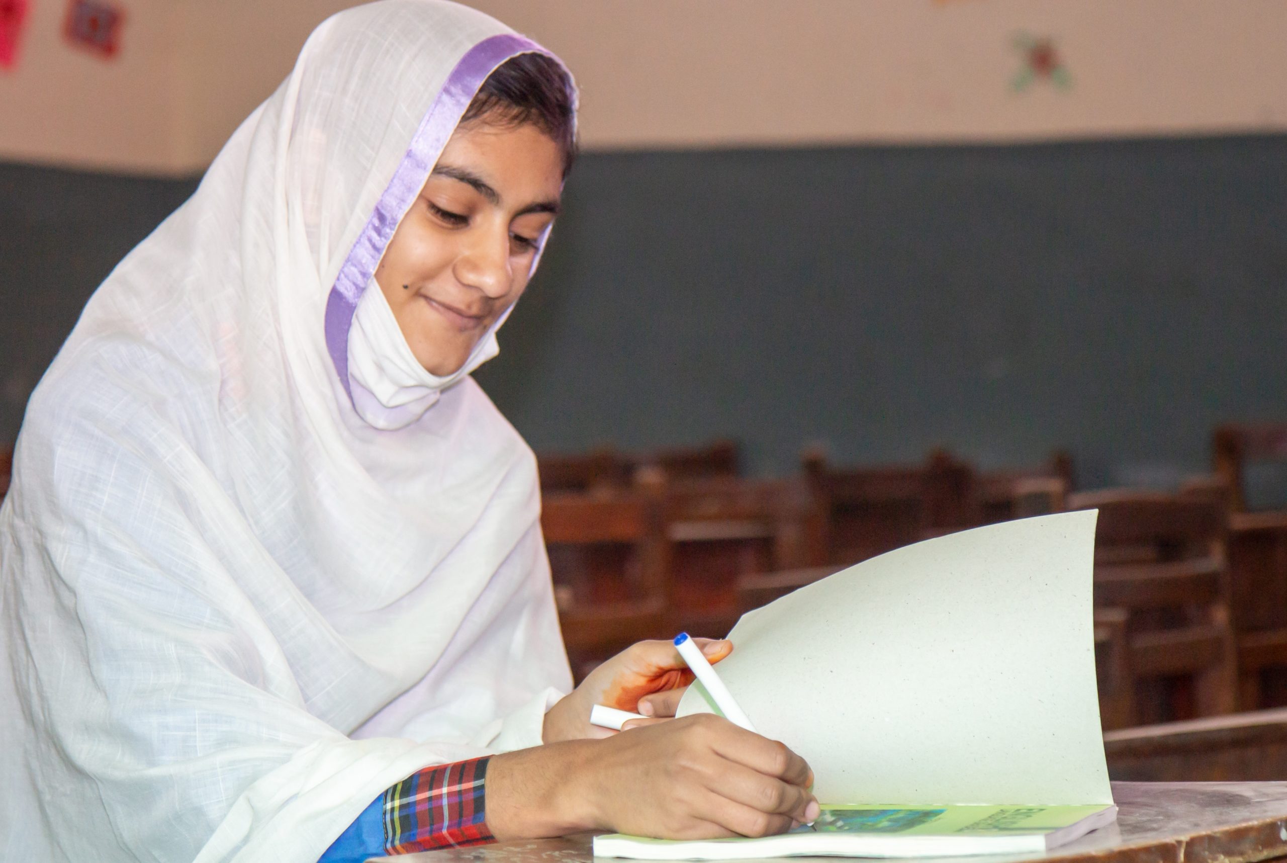 A school girl in Pakistan sitting in a classroom and writing something in a workbook