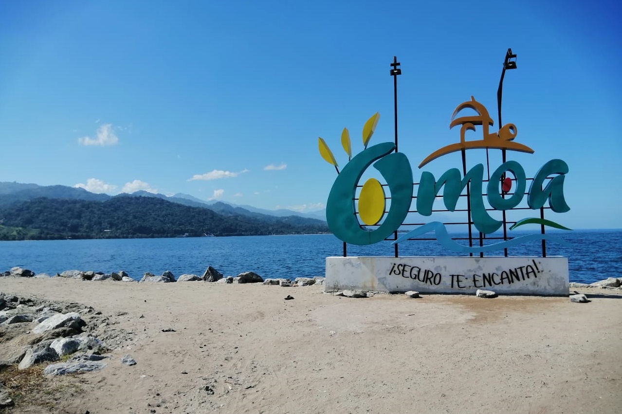 An Omoa sign in front of the blue sea and a blue sky