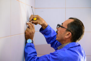 A man wearing a blue overall puts something on a wall