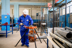 Ein Mann im blauen Overall steht in einer Werkstatt und arbeitet an einem Gerät.