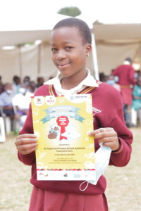 Una escolar ugandesa sostiene un certificado y sonríe a la cámara.