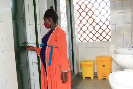A pregnant woman wearing an orange bathrobe enters a toilet cabin